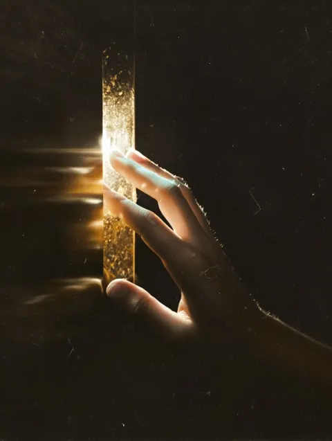 Dark cinematic close-up of a hand reaching toward a bright light source