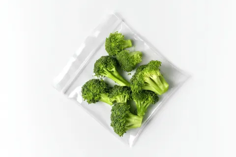 Overhead photo of bright green broccoli florets inside a clear shiny ziplock bag