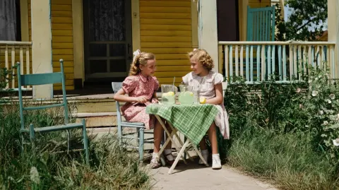 Girls selling lemonade at a stand in front of their porch, 40s style, colorized