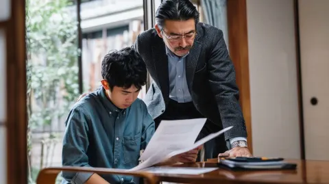 A 45-year-old Japanese man standing over his younger brother with a strict expression