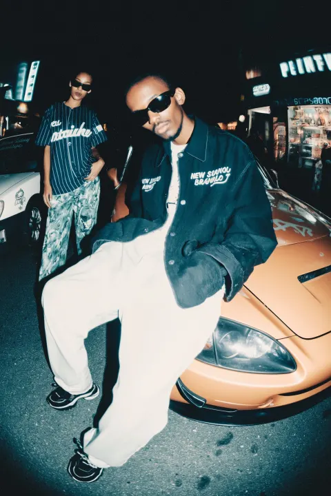 A young man in the foreground is wearing an open jacket with "new york brasileiro" embroidery
