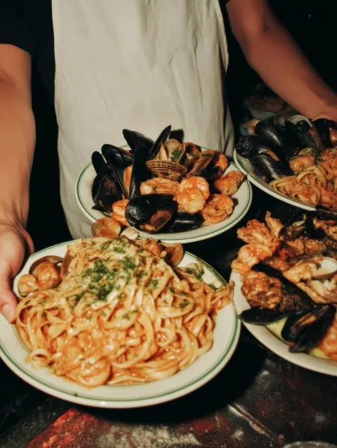 A server in a white apron is holding 3 plates of authentic italian food. shot on film with a bright