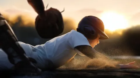 A silent Japanese high school baseball player sliding into home plate at sunset