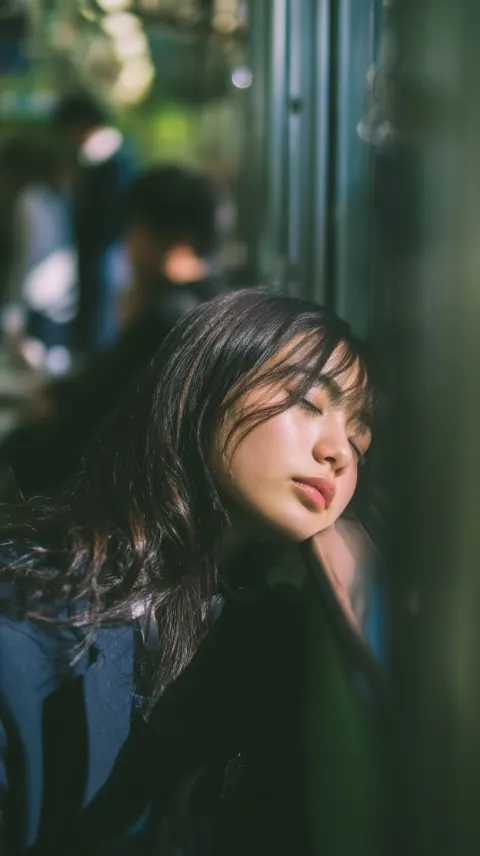 A natural, documentary-style photograph of a cute Japanese high school girl lightly dozing on a movi