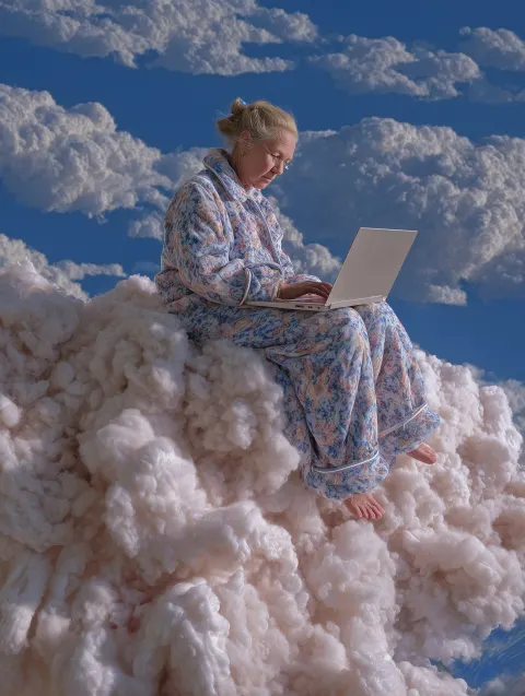 A young girl in pajamas sits on a cloud and types on her laptop