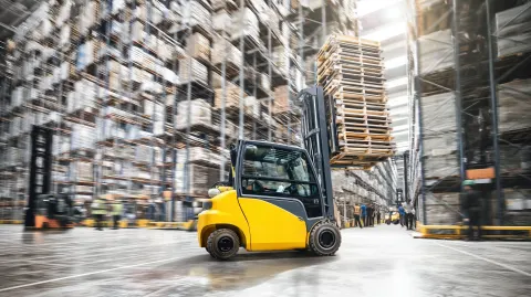 Detailed yellow industrial forklift carrying heavy wooden pallets driving through a massive bustling