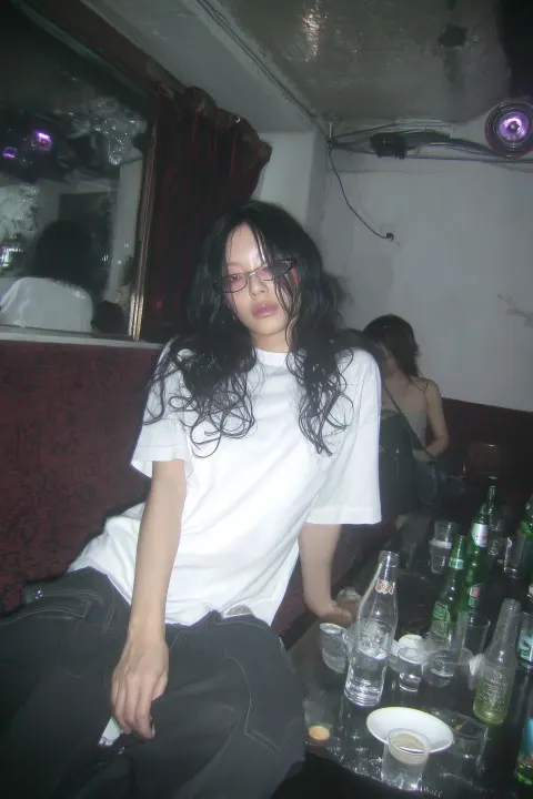 A candid flash photograph of an awkward nerdy Asian woman in her 20s with medium-length black curly