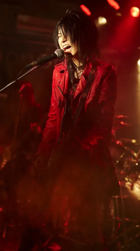 Realistic live music photograph of a young Japanese female hard rock guitarist-vocalist performing o