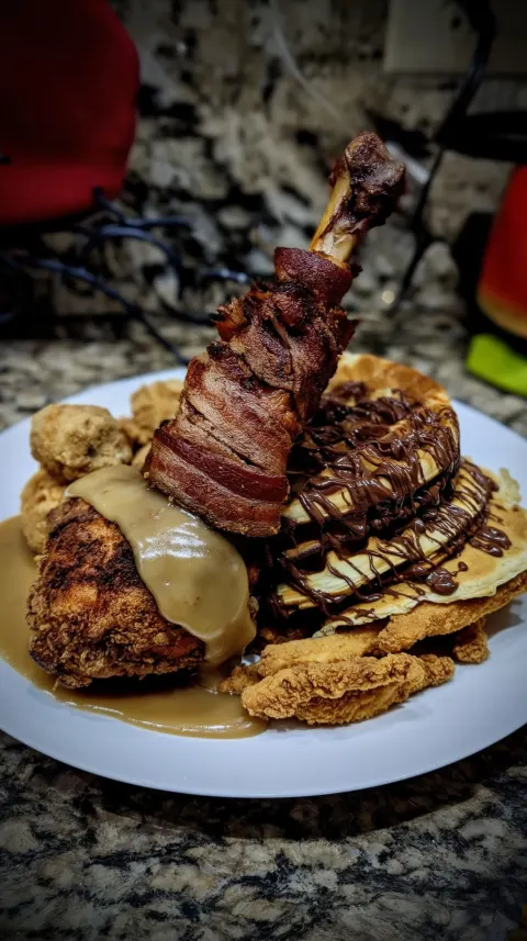 Fried chicken accompanied by a turkey leg covered in bacon smothered in gravy with several stacks of