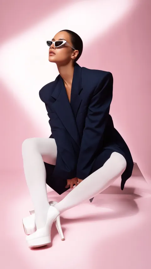 Full body fashion portrait of a stylish elegant woman sitting in a confident crossed-leg pose on an