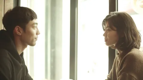 Korean young man and Korean young woman sitting diagonally across a small café table near a window