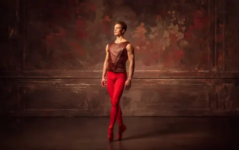 Male ballet dancer standing still, wearing a leather tunic and fiery red tights