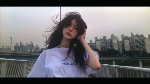 A beautiful Kpop young woman walking on a bridge using a white shirt saying "THIS IS US"