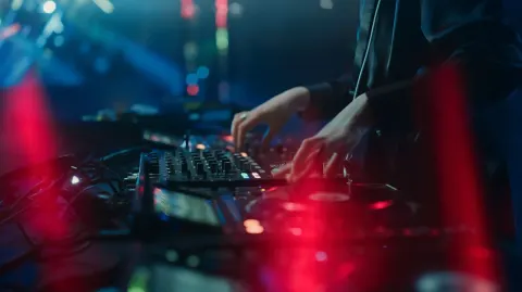 Modern DJ performing in a dark stylish nightclub, colorful neon lights and spotlights reflecting off