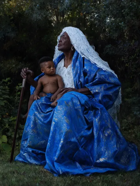 Nigerian elderly woman looking away, dressed in voluminous royal blue drapery with gold highlights a