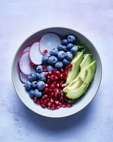 Bright spring superfood salad bowl featuring avocado wedges, blueberries, pomegranate seeds