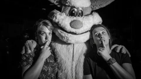 Two normal people posing with a mascot, but the mascot feels unsettling and too real