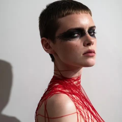 Female with dark makeup and short boycut hair. Shes wearing very thin red string around her body. St