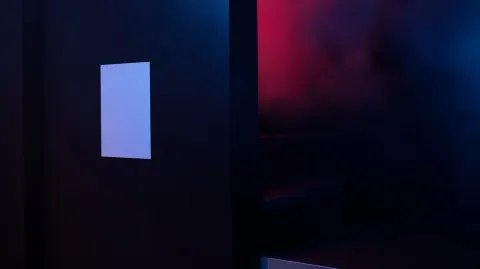 Straight-on shot of a vertical A3 white poster affixed to a black painted wall inside a nightclub. T