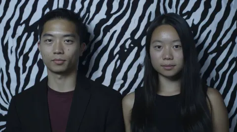 One asian man and one asian woman standing side by side, facing camera, neutral calm expressions