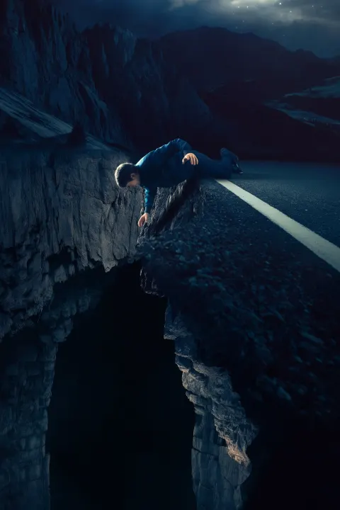 A person slipping off a mountain road cliff at night, body half over the edge