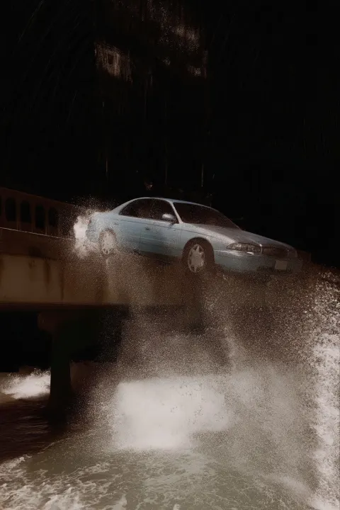 A silver sedan crashing in the sea from a bridge. black background