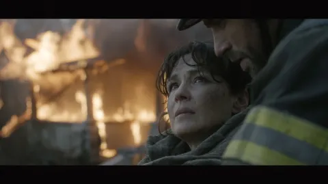 An exhausted, dirty-faced middle-aged woman has just escaped a fire with her burning house in the ba