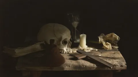 Caravaggesque vanitas still life, dark and austere composition. On a rough wooden table lie a human