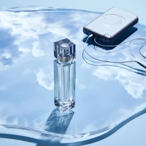 Glass luxury cosmetic bottle standing tall on a translucent undulating acrylic sheet acting as a sky
