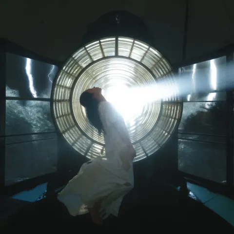 A young woman with long black hair and a tattered, torn white wedding dress is levitating in the air
