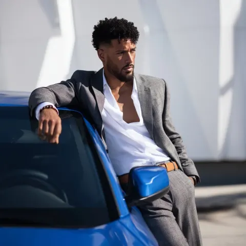 Photography of a latin man, leaning casually on a sleek blue city car