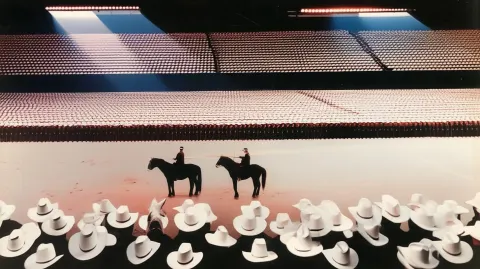 A wide shot among the crowd for 2 men on a black horses holding billiard sticks and playing in a sta