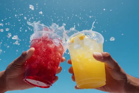 Two hands clinking together two clear plastic cups, placed at the bottom of the image against a brig