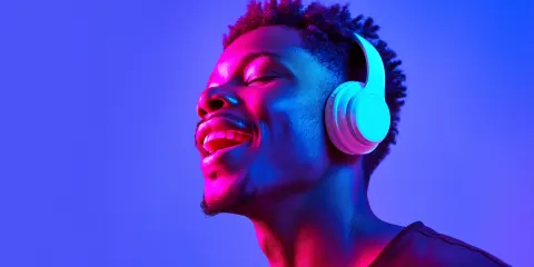 Young man wearing headphones enjoying music under neon pink and blue lighting, expressive emotion